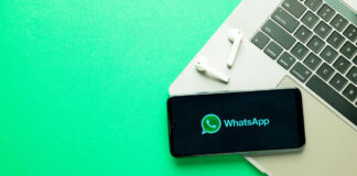 Smartphone on laptop with WhatsApp displayed alongside earbuds