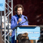 A woman in a blue suit speaking at a podium during a political rally