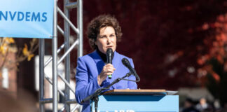 A woman in a blue suit speaking at a podium during a political rally