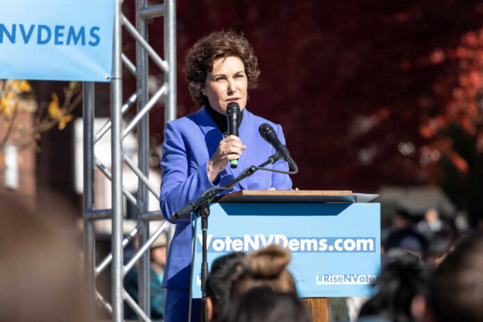 A woman in a blue suit speaking at a podium during a political rally