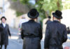 Two men in traditional black attire and hats walking down a street