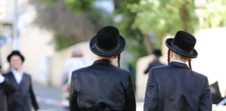 Two men in traditional black attire and hats walking down a street
