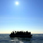 Silhouetted figures on a boat in the ocean under a bright sun