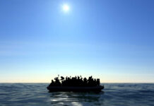 Silhouetted figures on a boat in the ocean under a bright sun