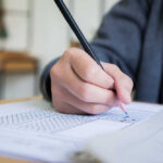 A student's hand holding a pencil while filling out a test paper