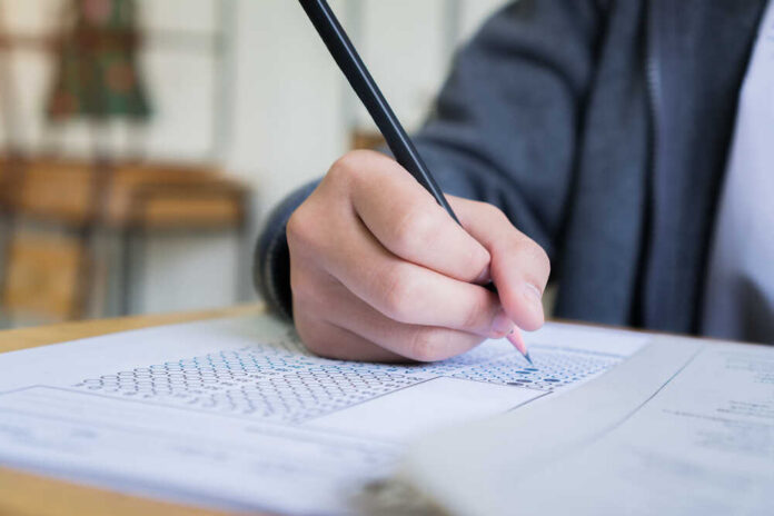 A student's hand holding a pencil while filling out a test paper