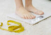 Person standing on a digital scale with a measuring tape nearby
