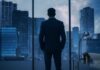 A man in a suit standing in an office looking out at a city skyline