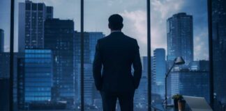 A man in a suit standing in an office looking out at a city skyline