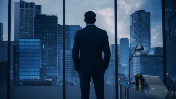 A man in a suit standing in an office looking out at a city skyline