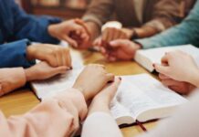 Group of hands holding each other over an open Bible