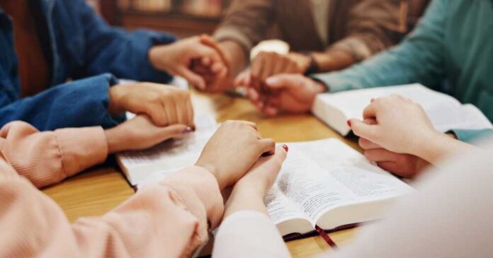 Group of hands holding each other over an open Bible