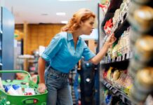Woman shopping in a supermarket aisle, examining products on the shelf