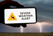 A hand holding a smartphone displaying a severe weather alert against a stormy background