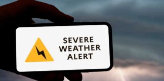 A hand holding a smartphone displaying a severe weather alert against a stormy background