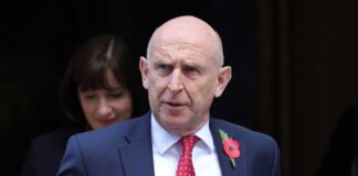 A man in a suit with a red tie and poppy flower, walking outdoors