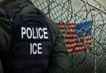 Police officer in tactical gear standing near a barbed wire fence with an American flag in the background