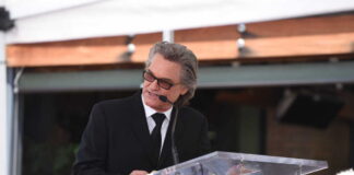 A man in a black suit delivering a speech at a Hollywood event