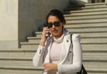 Person in white jacket talking on phone, wearing sunglasses.