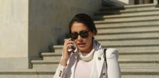 Person in white jacket talking on phone, wearing sunglasses.
