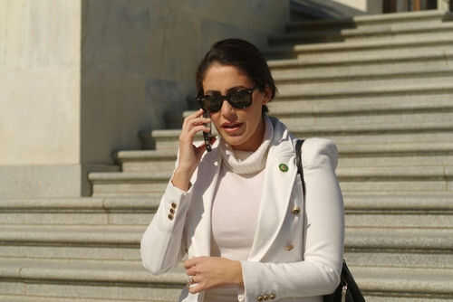 Person in white jacket talking on phone, wearing sunglasses.