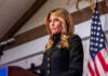 First Lady’s Fiery Speech Ignites Political Firestorm Woman speaking at podium with American flag background
