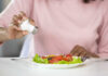 Person adding salt to a fresh salad on a plate