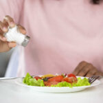 Is Your Diet Speeding Up Vascular Aging? Person adding salt to a fresh salad on a plate