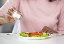 Person adding salt to a fresh salad on a plate