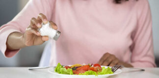 Person adding salt to a fresh salad on a plate