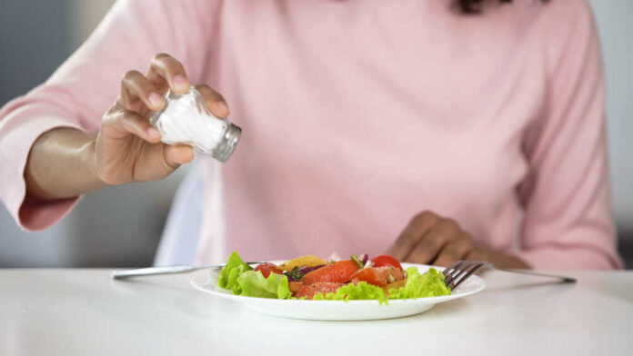 Person adding salt to a fresh salad on a plate