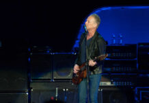 A guitarist performing on stage with amplifiers in the background