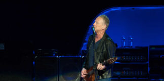 A guitarist performing on stage with amplifiers in the background