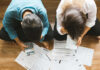 A couple sitting on the floor surrounded by financial documents and a calculator