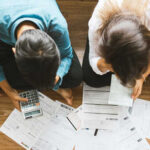 A couple sitting on the floor surrounded by financial documents and a calculator