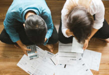 A couple sitting on the floor surrounded by financial documents and a calculator
