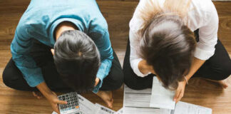 A couple sitting on the floor surrounded by financial documents and a calculator