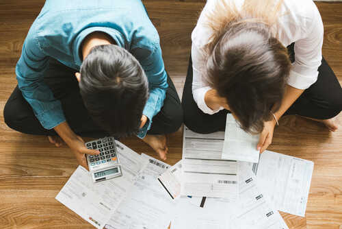 A couple sitting on the floor surrounded by financial documents and a calculator