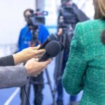 Hands holding microphones in front of a person at a press conference