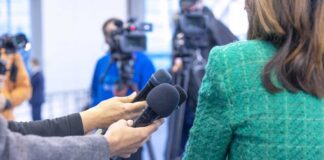 Hands holding microphones in front of a person at a press conference
