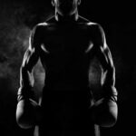 Silhouette of a muscular boxer holding gloves in a dark setting
