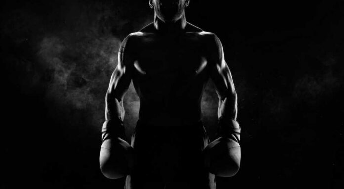Silhouette of a muscular boxer holding gloves in a dark setting