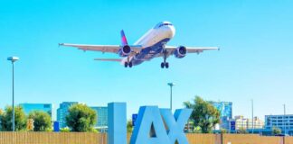 An airplane approaching LAX airport with the airport sign in the foreground