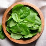 Fresh spinach leaves in a wooden bowl on a linen surface
