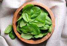 Fresh spinach leaves in a wooden bowl on a linen surface