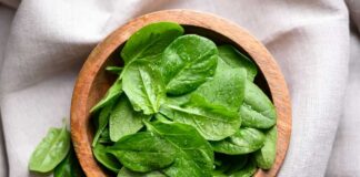 Fresh spinach leaves in a wooden bowl on a linen surface