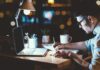 Person writing notes at a desk with a laptop and a warm light