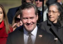 A smiling man in a suit at a political event surrounded by a crowd