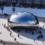 A large, reflective sculpture in a city park with people gathered around it
