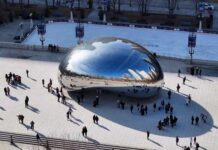 A large, reflective sculpture in a city park with people gathered around it